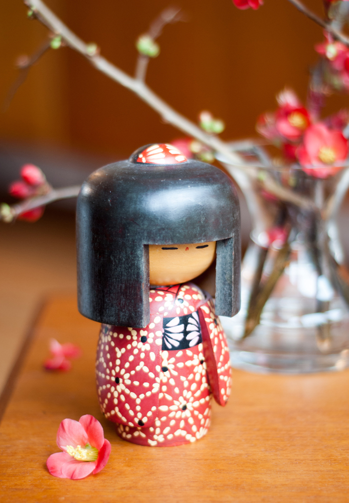 Rote Blüten der Zierquitte in der Vase mit japanischer Koskeshi Puppe