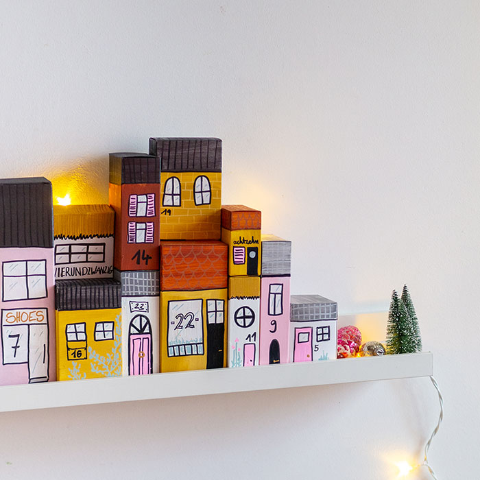 Aus Papp-Verpackungen (zum Beispiel von Lebensmitteln) kannst du mit ein bisschen Farbe und Fantasie einen tollen DIY Adventskalender basteln. Die upcycling Häuserzeile ist zudem noch eine tolle, weihnachtliche Dekoration.